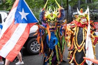 Two people dressed in costumes walk down the street with Puerto Rico flags 