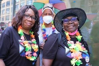 Three women pose for a photo. The woman in the middle is wearing a mask. 