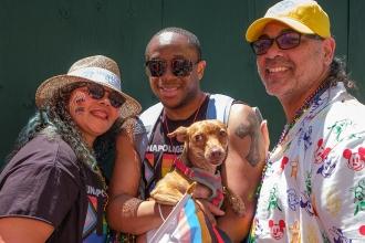 Three people pose while holding a dog 