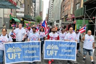 A large group of members wearing Puerto Rican flag colors and holding UFT signs march down a street. 