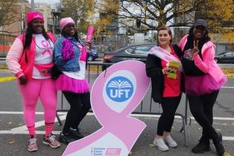 4 women pose alongside a breast cancer ribbon. 