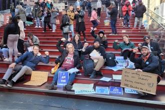 A group of teachers sit on the Times Square steps and raise their fists. 