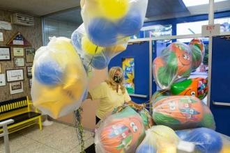 A teacher has her hands full of balloons that are inflated and in garbage bags. 