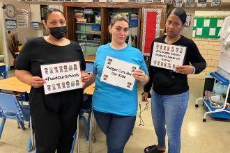 Three women hold up signs in a classroom