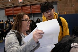 A woman explains contents of a paper to a student at a college fair. 