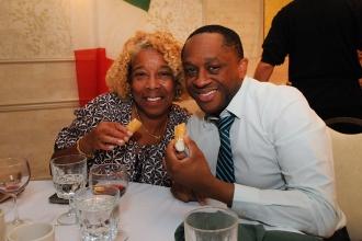 A man and woman smile at a table while holding cannolis 