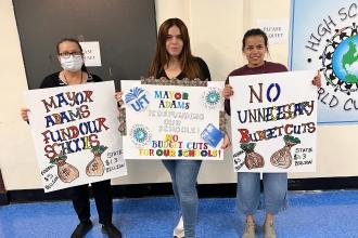 Three women hold up signs in a hallway 
