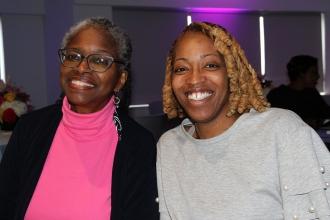 Two women smile in front of a camera 