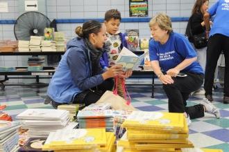 A woman and her child look at books and talk with another woman in a blue shirt