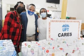 A man and two women pose for a photo while wearing masks behind a distribution table. 