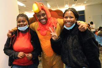 Three people pose for a photo. The man in the middle is wearing a turkey costume.