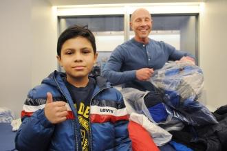 A student gives a thumbs up and an adult donating coats smiles behind him.