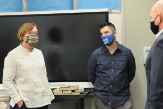 A woman turns to talk to two men in a classroom. All are wearing masks.