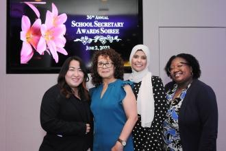 4 women pose for a photo in front of a television screen reading "36th annual School Secretary Awards Soiree"