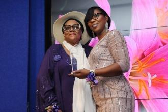 A woman on the right presents the woman on the left with an award as they both smile for a photo. 