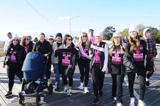 A group of marchers walk down a boardwalk wearing black and pink shirts 