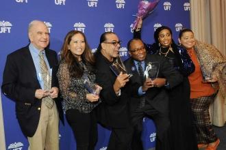 A group of award winners pose in front of a UFT backdrop