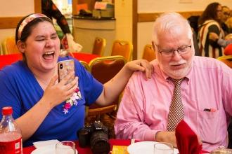 A woman and man laugh while recording the events at the celebration. 