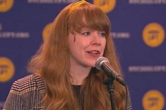 Woman stands at podium and asks a question through a microphone