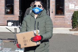 A woman walks outside of a building with a box of food.