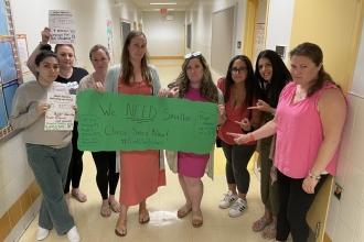 A group of teachers hold a sign together in a hallway
