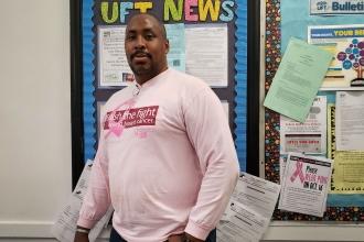 Randolph Hill, a paraprofessional at the school shows off his pink shirt in front of a UFT News bulletin board. 
