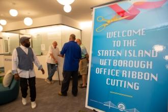Four men stand in an office lobby. A sign reads "Welcome to the Staten Island UFT Borough Office Ribbon Cutting."