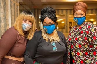 Three women pose for a photo while wearing masks