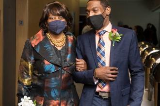 A woman walks side by side with a man, both wearing masks. 