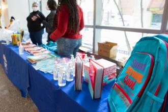 Volunteers stand ready behind a table with books, a backpack and hand sanitizer