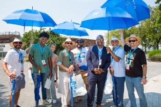 A group holding blue umbrellas outside in a park, lined up and smiling 