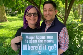 A woman and a man pose for a photo at a rally against budget cuts outside New York City Hall. They hold up a poster saying "Mayor Adams says he spent the money. Where'd it go?".