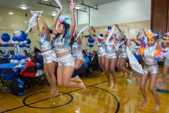 Cheerleaders with arms in the air jumping leads students from four Brooklyn schools in a steel drum band.
