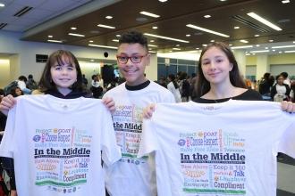 3 students holding T-shirts that say "In the Middle"