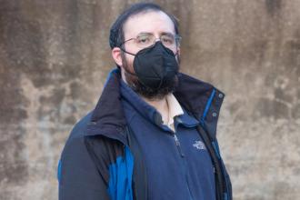 Samuel Berck takes a photo at a public schoolyard. He is standing and wearing a black N95 mask