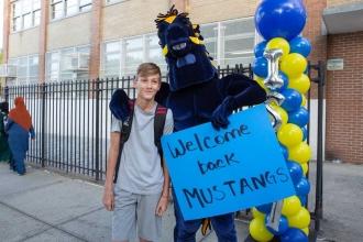 A student stands next to a mascot in a mustang costume