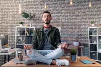Man meditating while sitting on top of his desk at work