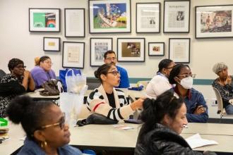 A woman sitting in a room full of parents asks a question while sitting at a table