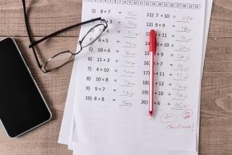 Paper with math problems, a pen, a smartphone and glasses