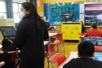 Image of students and teacher in a classroom. The teacher is wearing a mask