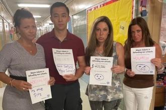 Four UFT members hold up posters that say "Mayor Adams is defunding our schools. Our school could lose up to $400,000." Written underneath are sad crying faces or the phrase "it's the pits".