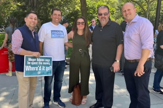 Four UFT Queens district representatives and one chapter advocate pose for a photo at a rally in City Hall Park. The man on the left holds a poster reading: "Mayor Adams says he spent the money. Where'd it go?".