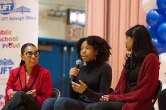 Three women on stage, one speaking into microphone