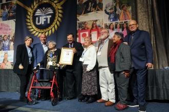 The family of the late Richard Miller, including his widow, retired educator Janet Miller (third from left), accept an In Memoriam plaque honoring the former UFT vice president, who died in May 2025, from Weingarten, Mantell (second from left) and Mulgrew (right).