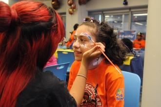 An 11-year-old student has her face painted by a Queens Technical HS student volunteer.