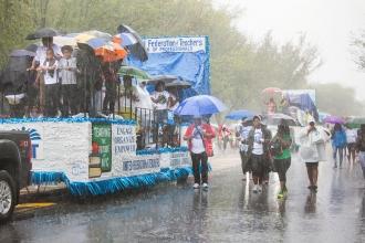 UFT float in the rain with members holding umbrellas walking alongside it