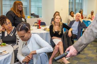 A group of attendees listen to a speaker while sitting at their tables