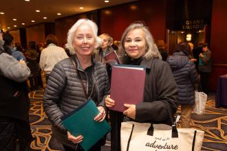 Two women smile for a photo with notebooks in their hands 