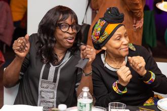Two women dance while sitting at a table