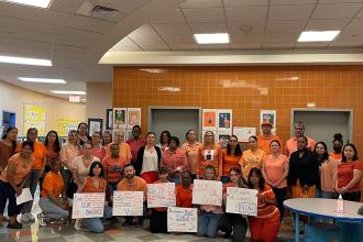 A group of staff members pose together wearing orange